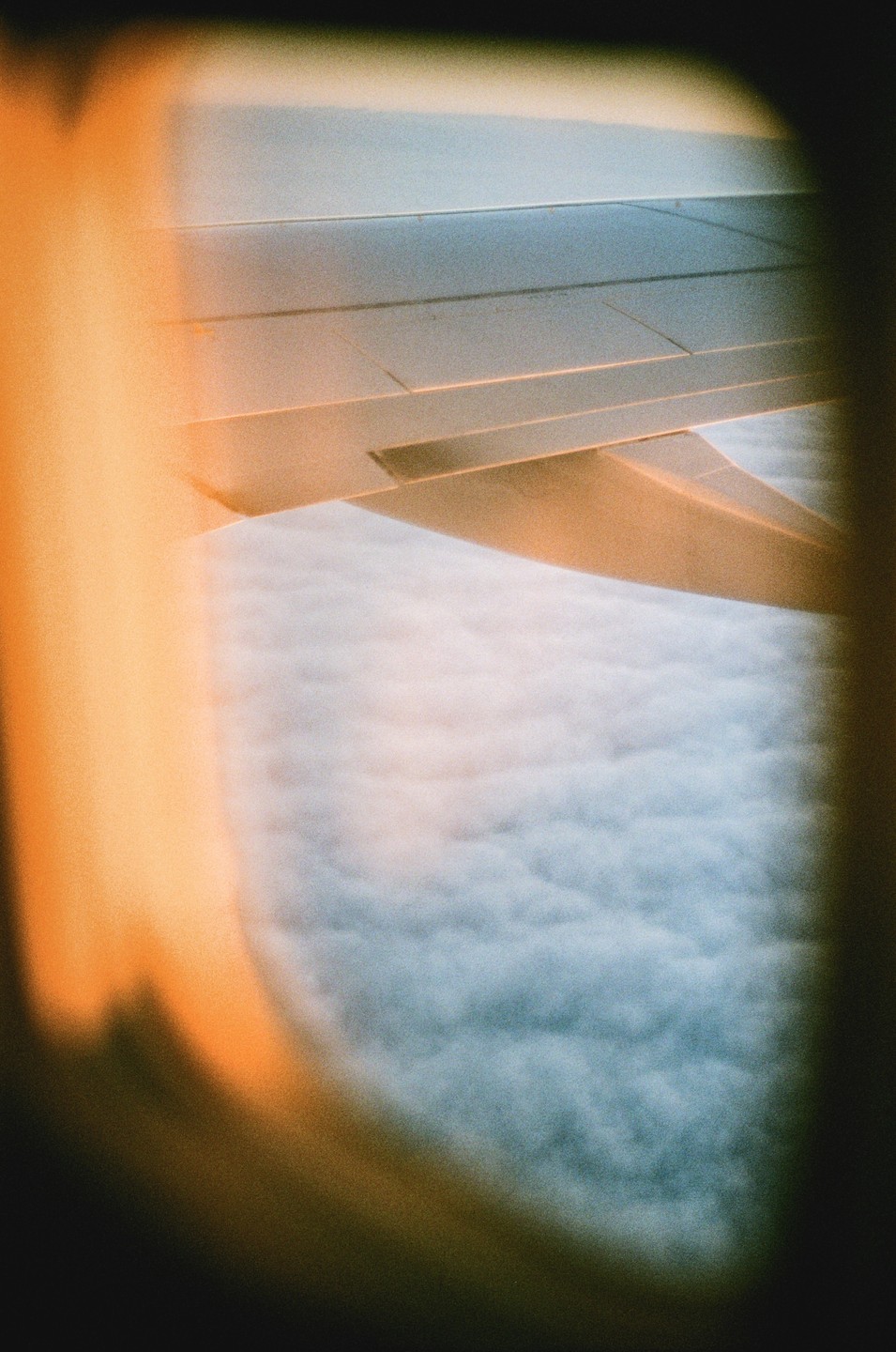 An airplane wing is visible above a layer of clouds, viewed from a window.