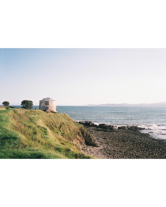 A stone tower stands on a grassy cliff overlooking a rocky beach and the ocean.