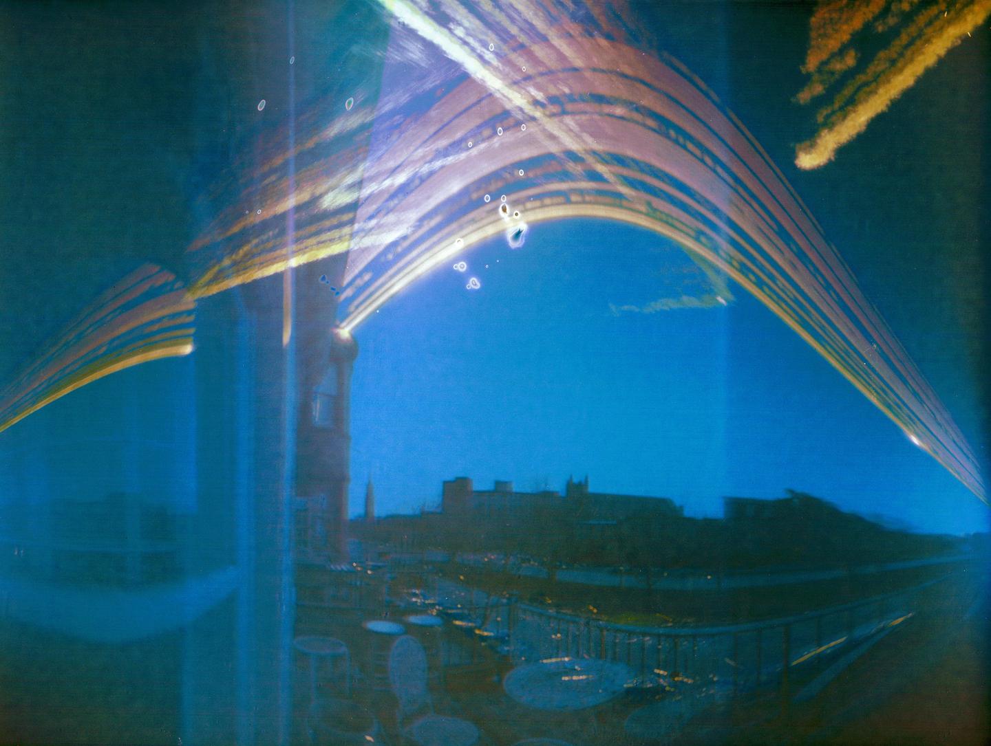 A long exposure shows light trails arcing over a city skyline at night.