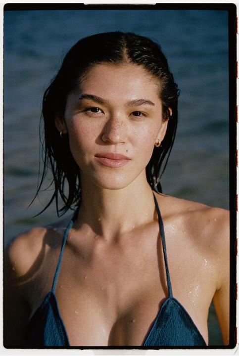 A woman with wet hair and freckles wears a blue bikini top in the water.