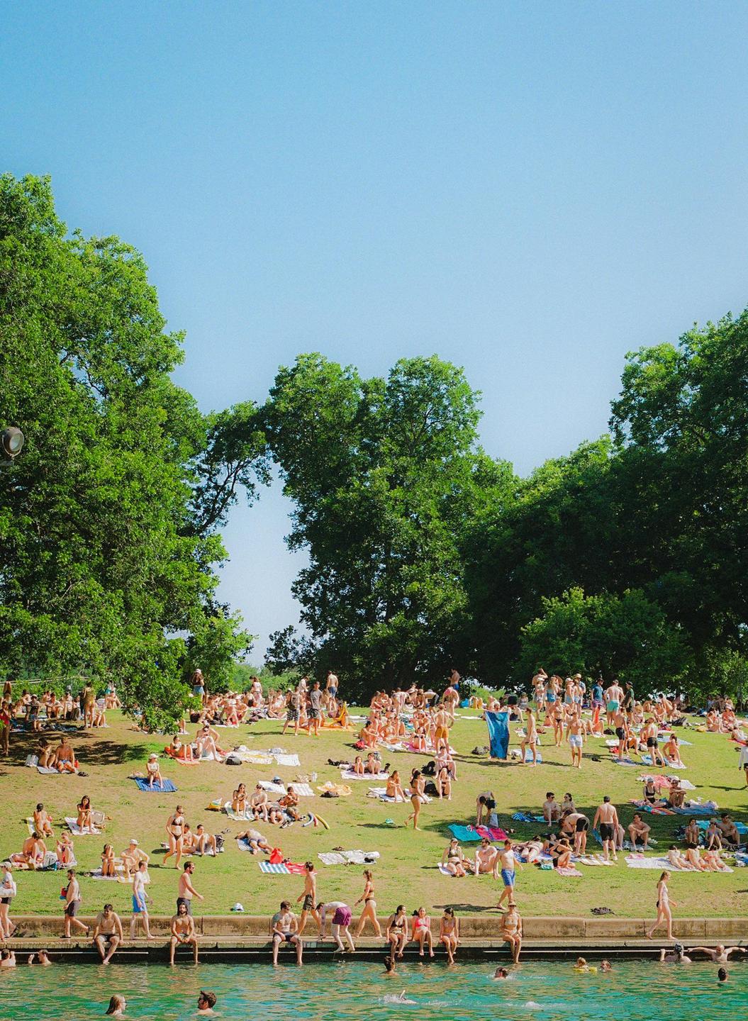 A large crowd of people are sunbathing and swimming in a natural pool on a sunny day.