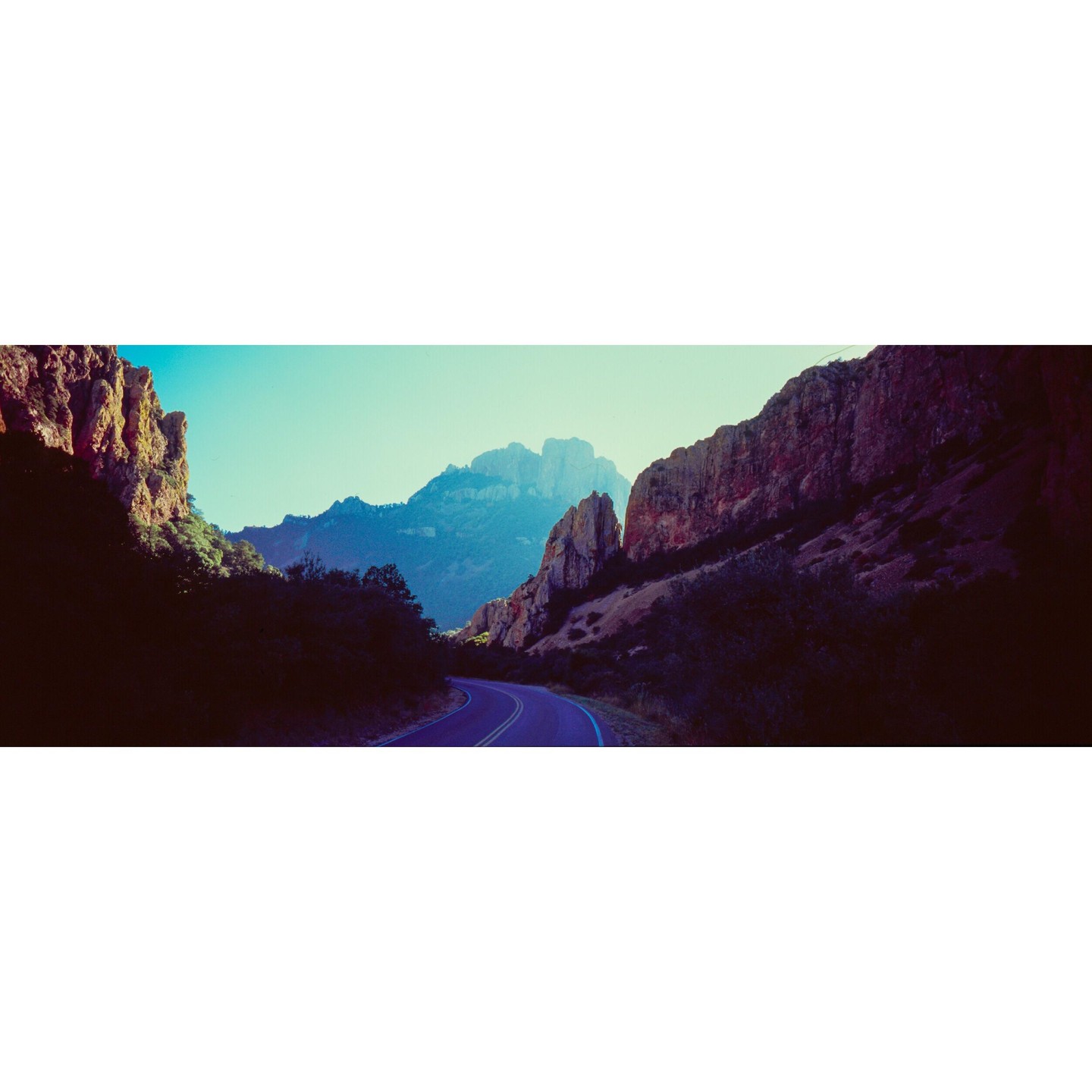 A winding road leads through a mountain pass with steep rock formations on either side.