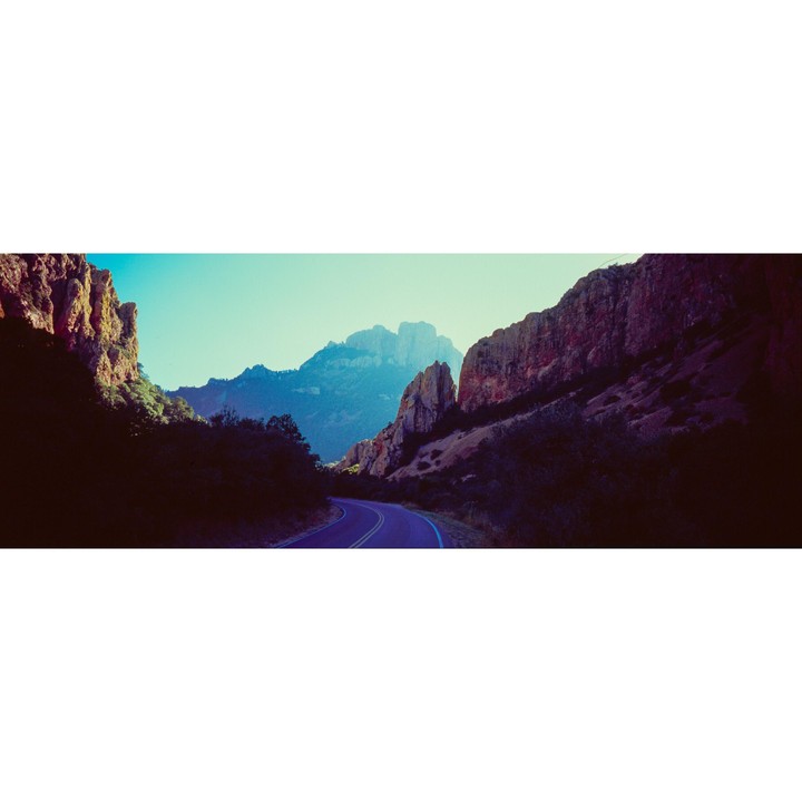 A winding road leads through a mountain pass with steep rock formations on either side.