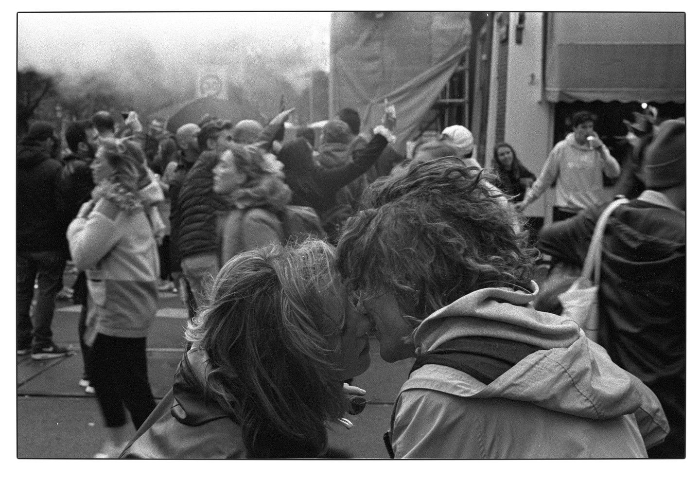 A couple kisses in a crowd of people on a street.
