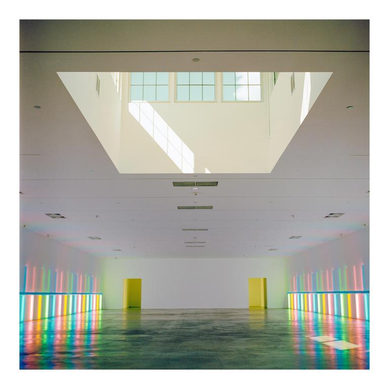 A large, empty room with a skylight and colorful neon lights reflecting on the floor is visible.