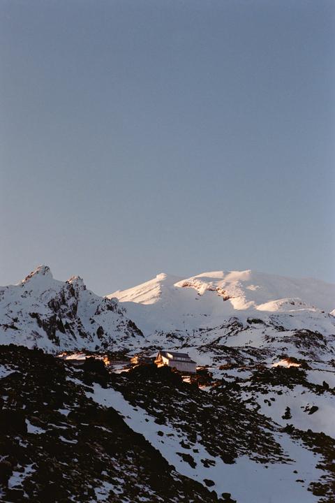 A small village with buildings and ski lifts is nestled in a snowy mountain landscape under a clear sky.
