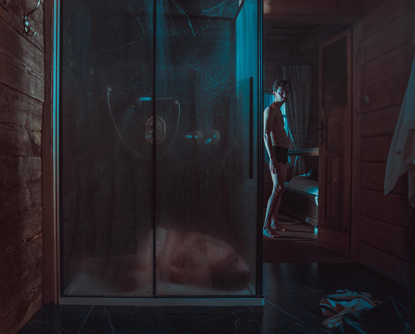 A man stands in a dark room next to a steamy shower stall.