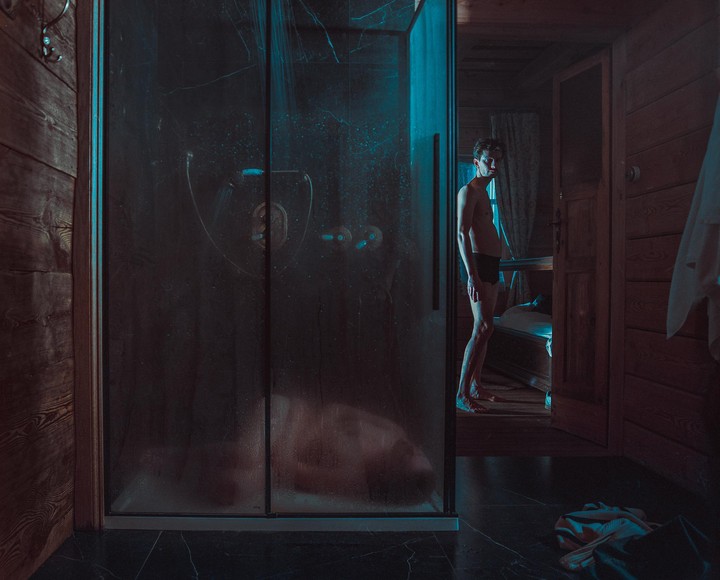 A man stands in a dark room next to a steamy shower stall.