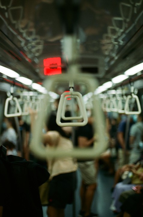 A blurry interior view of a subway car shows hanging hand straps and passengers.