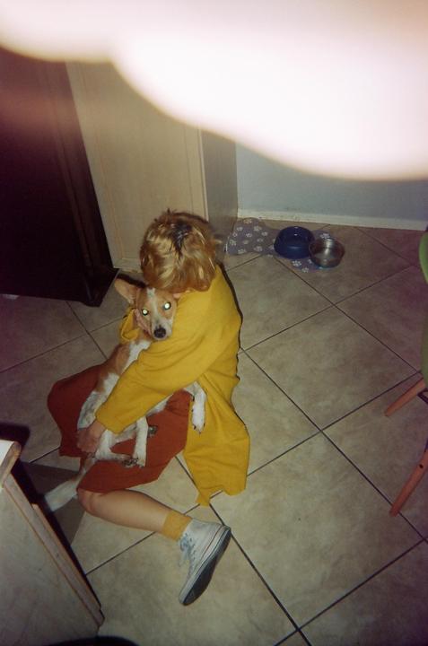 A person in a yellow top sits on a tiled floor, holding a dog with glowing eyes.
