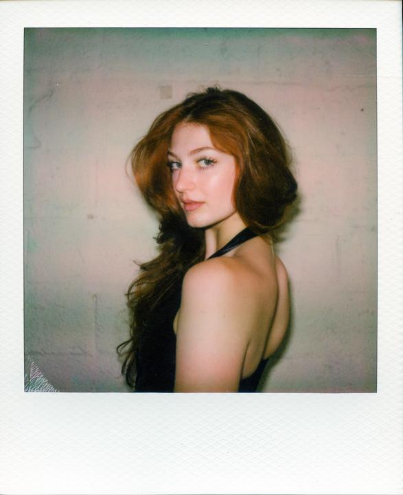 A woman with long red hair looks over her shoulder at the viewer.