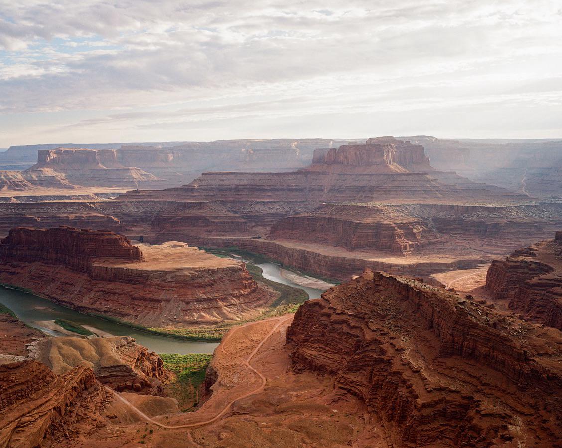 A wide river winds through a vast canyon landscape under a cloudy sky.
