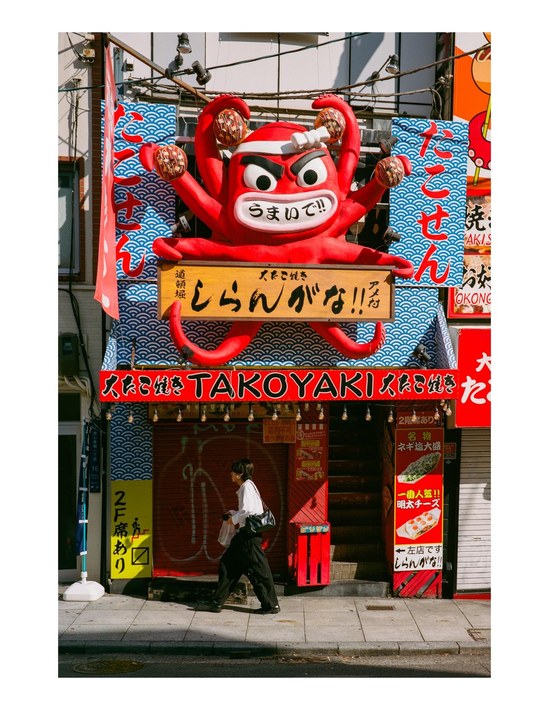 A person walks past a building with a large red octopus sculpture on its facade.