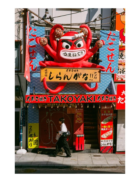 A person walks past a building with a large red octopus sculpture on its facade.