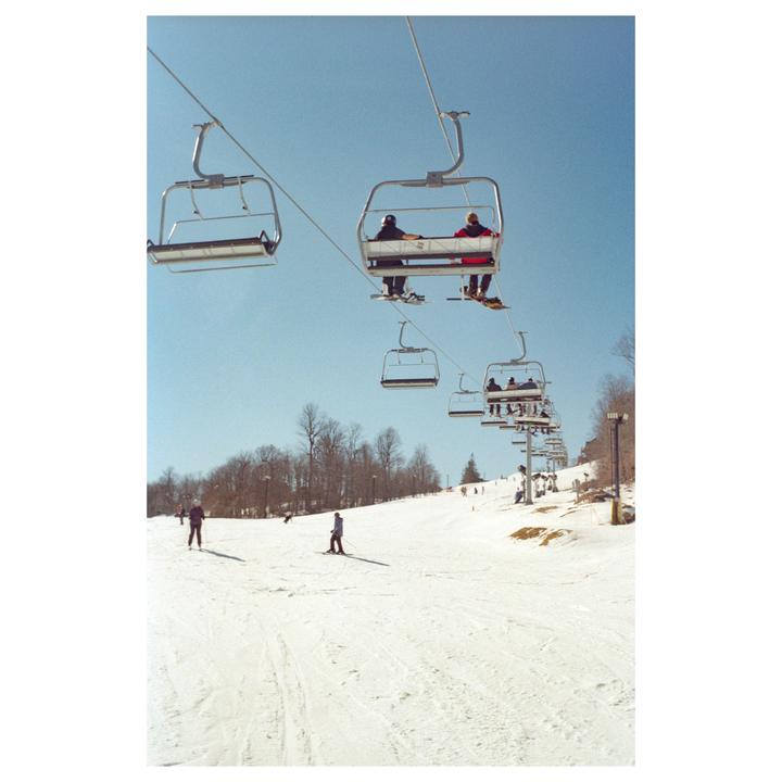 People are riding ski lifts and skiing down a snowy mountain slope under a clear blue sky.