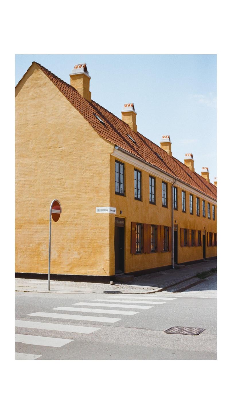 A row of yellow buildings with red tile roofs stands beside a street with a crosswalk and a stop sign.