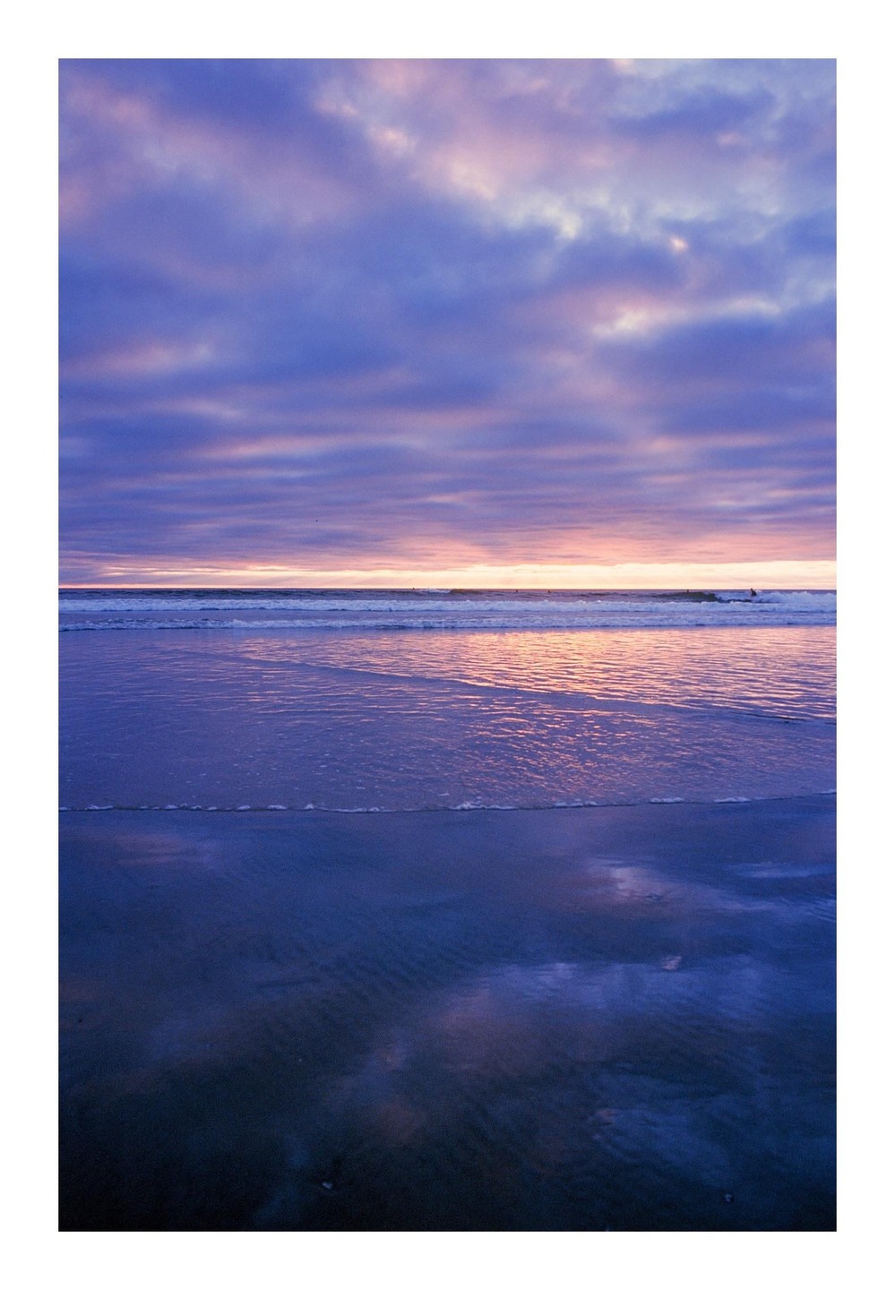 The ocean reflects the purple and pink hues of the sunset sky.