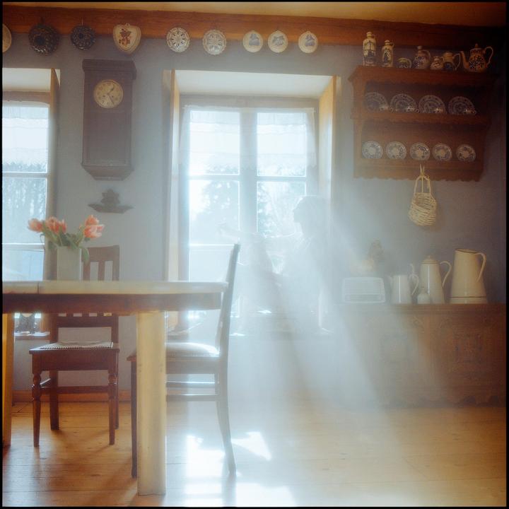 Sunlight streams through a window into a room with a table, chairs, and various decorative items.