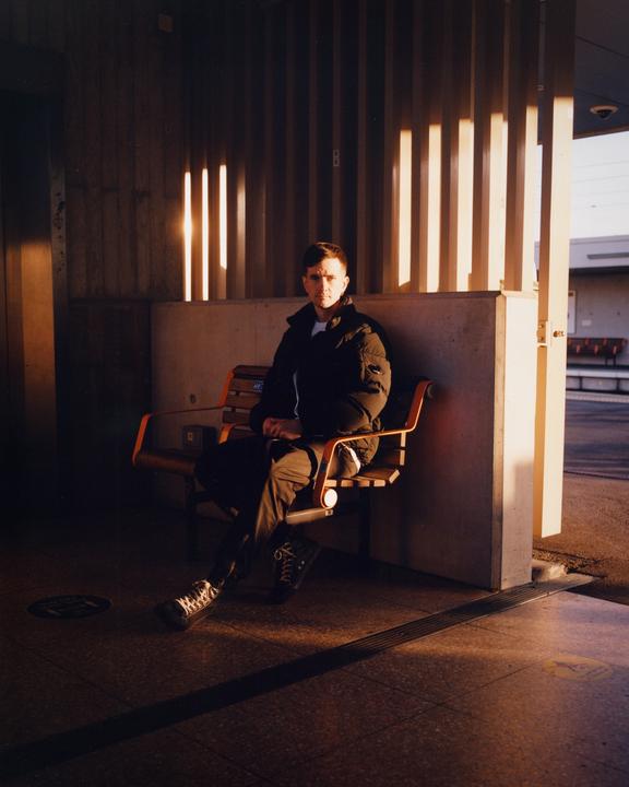 A man sits on a bench in a sunlit area with vertical shadows.