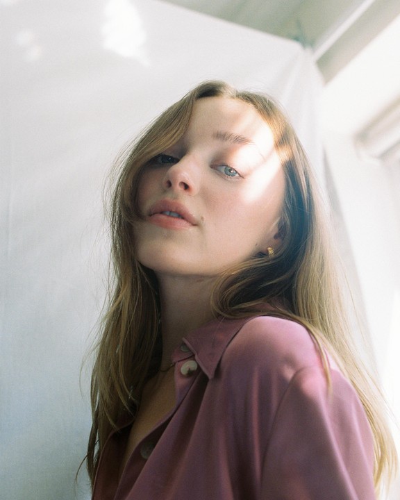 A woman with long hair and a pink shirt looks up at the camera with light stripes across her face.