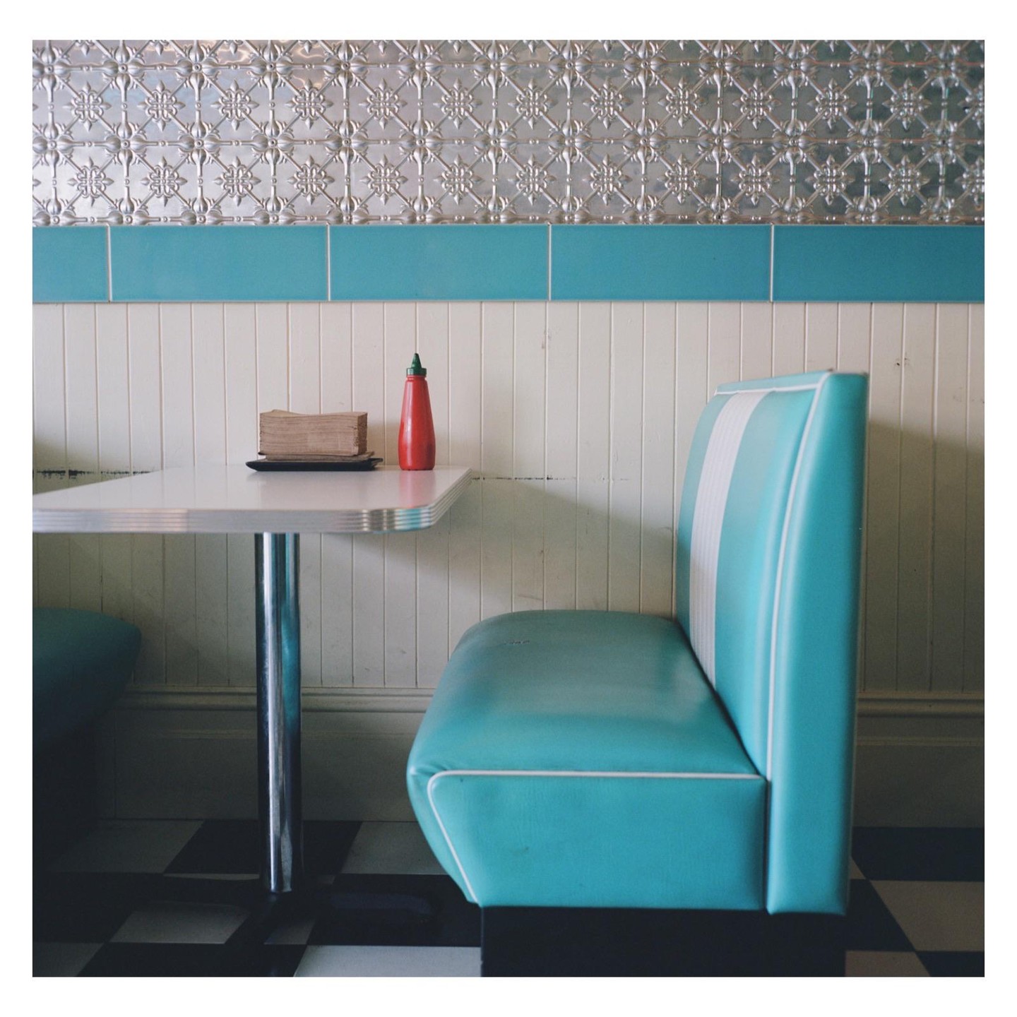 A diner booth with a turquoise seat and a table with a ketchup bottle and napkins is shown.