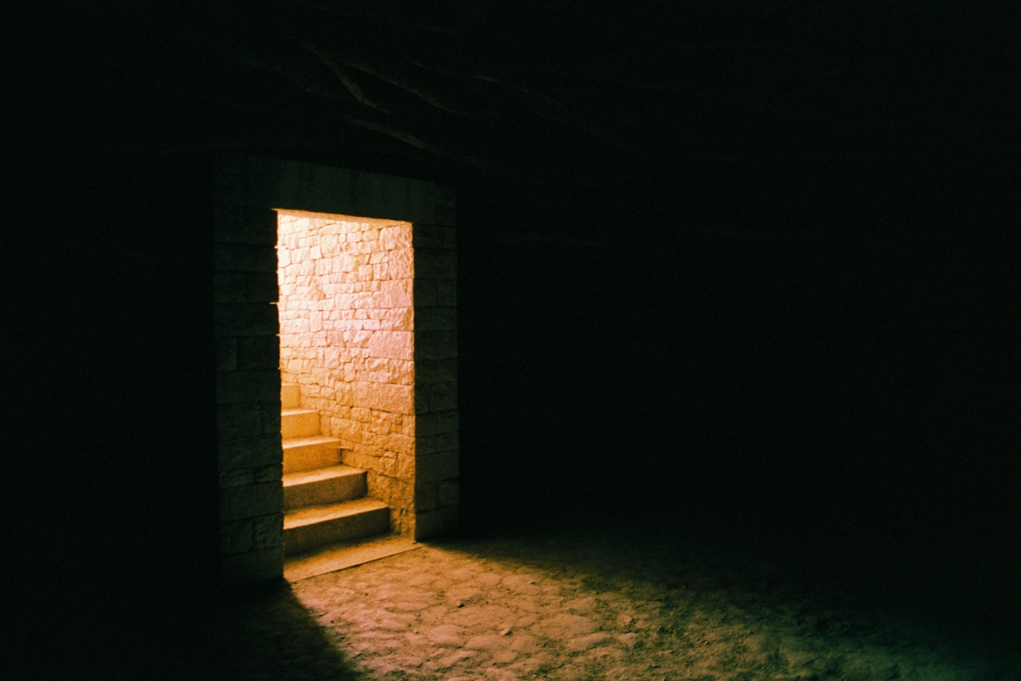 A stone doorway with steps leads into a brightly lit space from a dark room.
