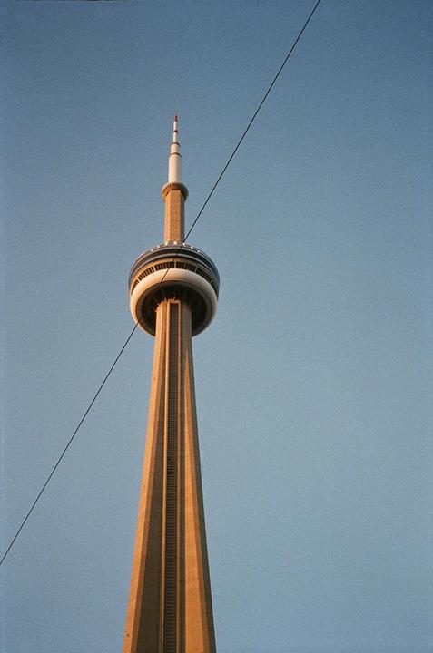 The CN Tower stands tall against a clear blue sky, with a diagonal wire crossing the frame.