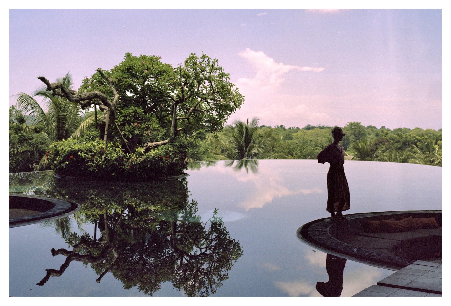 A woman stands at the edge of an infinity pool with a lush green landscape in the background.