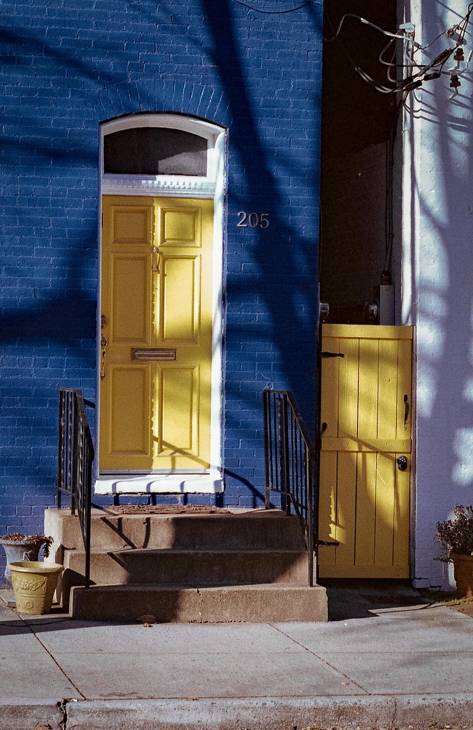 A bright yellow door is set into a blue brick wall next to a set of concrete steps with black railings.