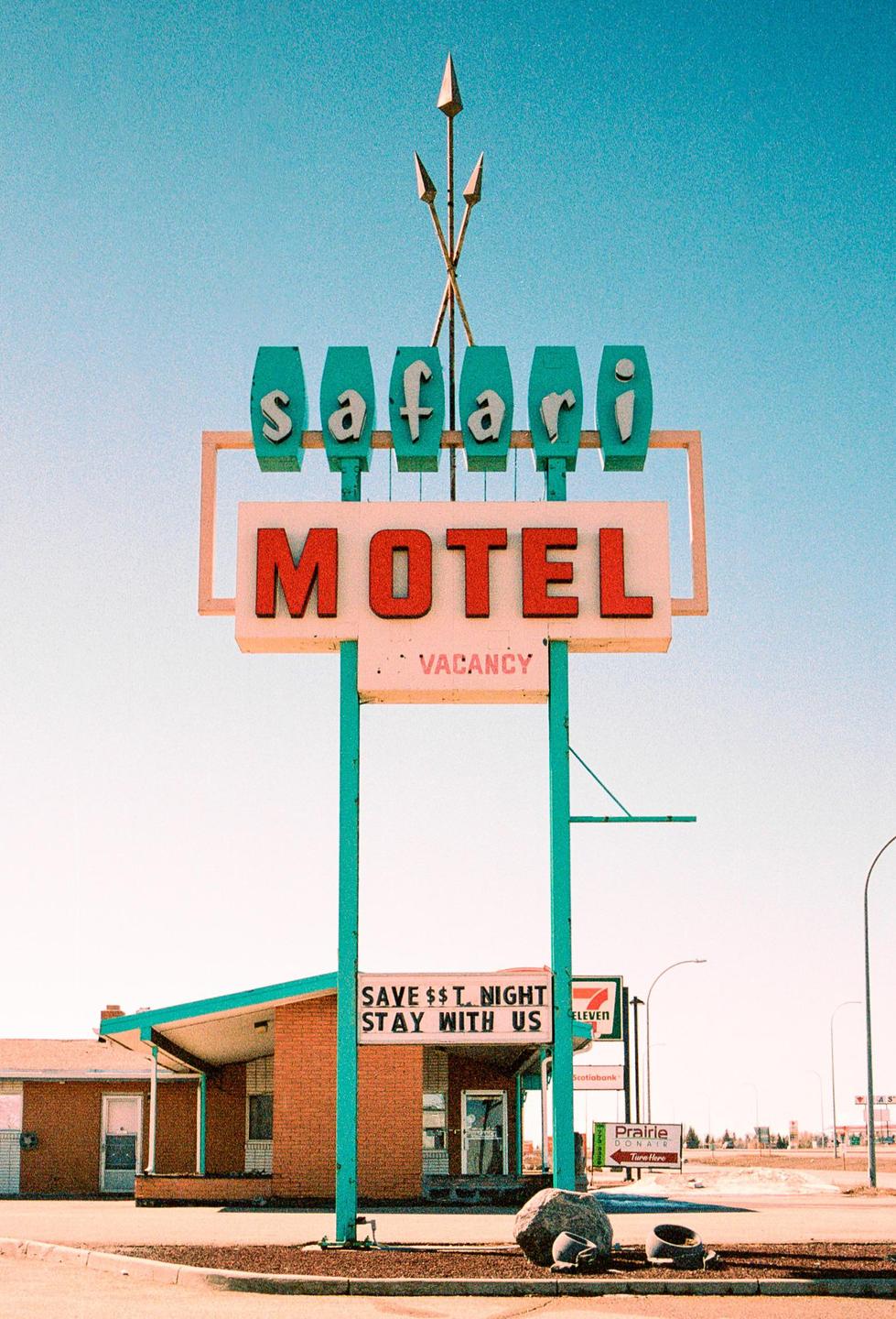 A large motel sign with the words "Safari Motel" and "Vacancy" stands in front of a brick building with a teal roof.