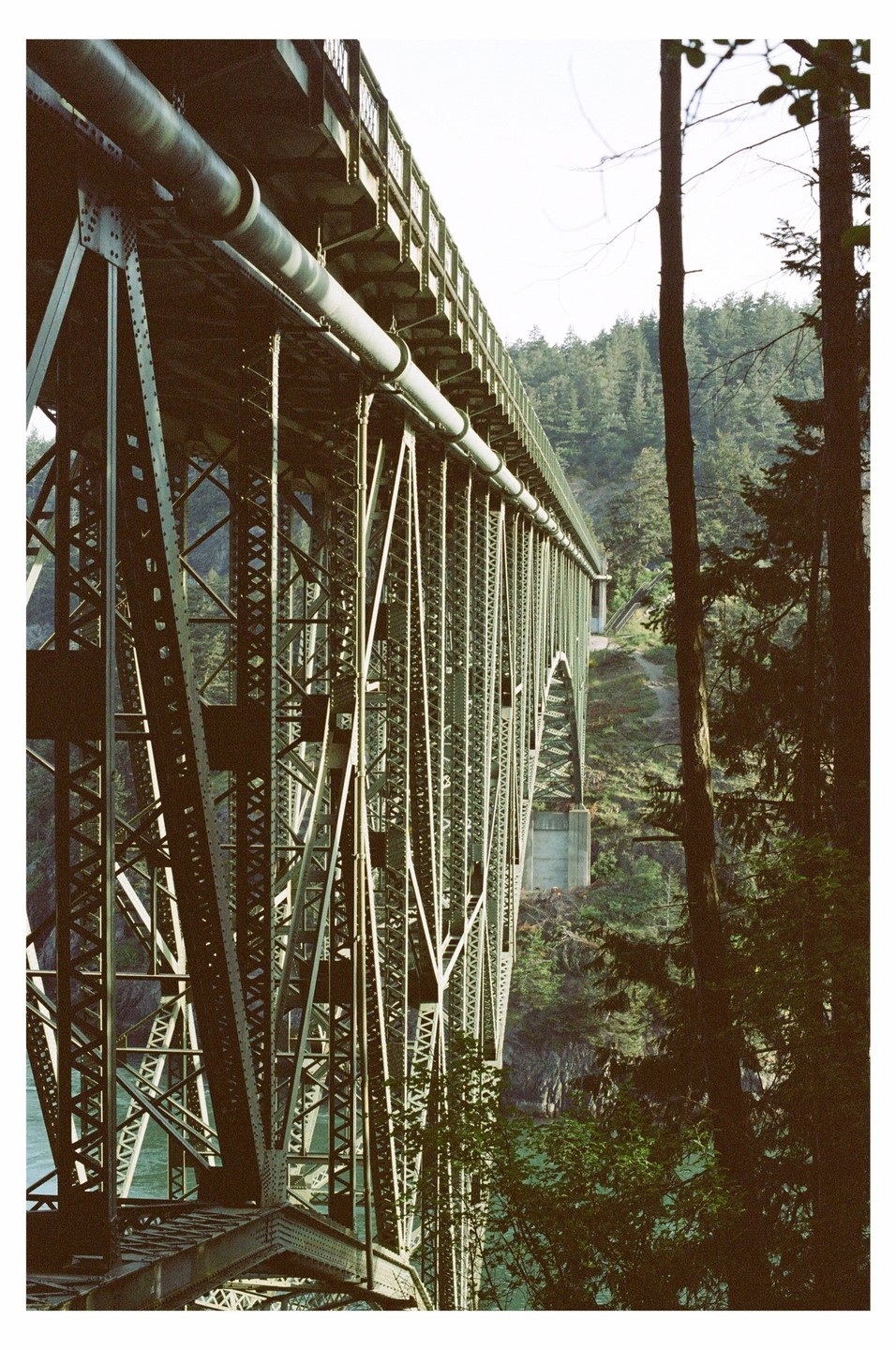 A large metal bridge spans a body of water with a forest on the far bank.