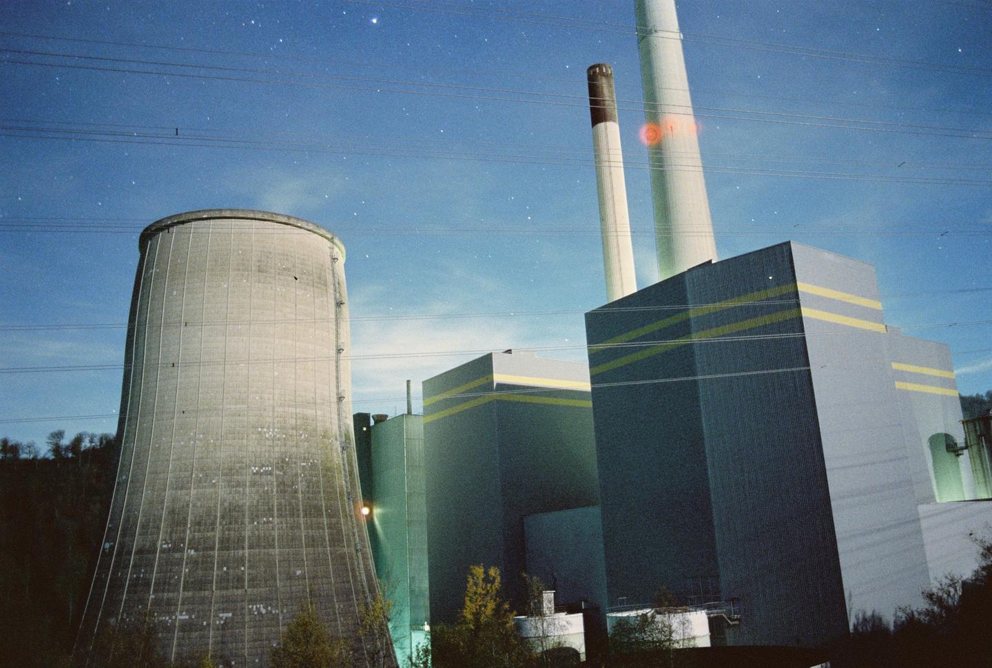 A large cooling tower and industrial buildings stand under a starry night sky.