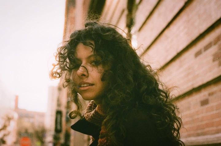 A woman with long curly hair looks over her shoulder at the viewer.