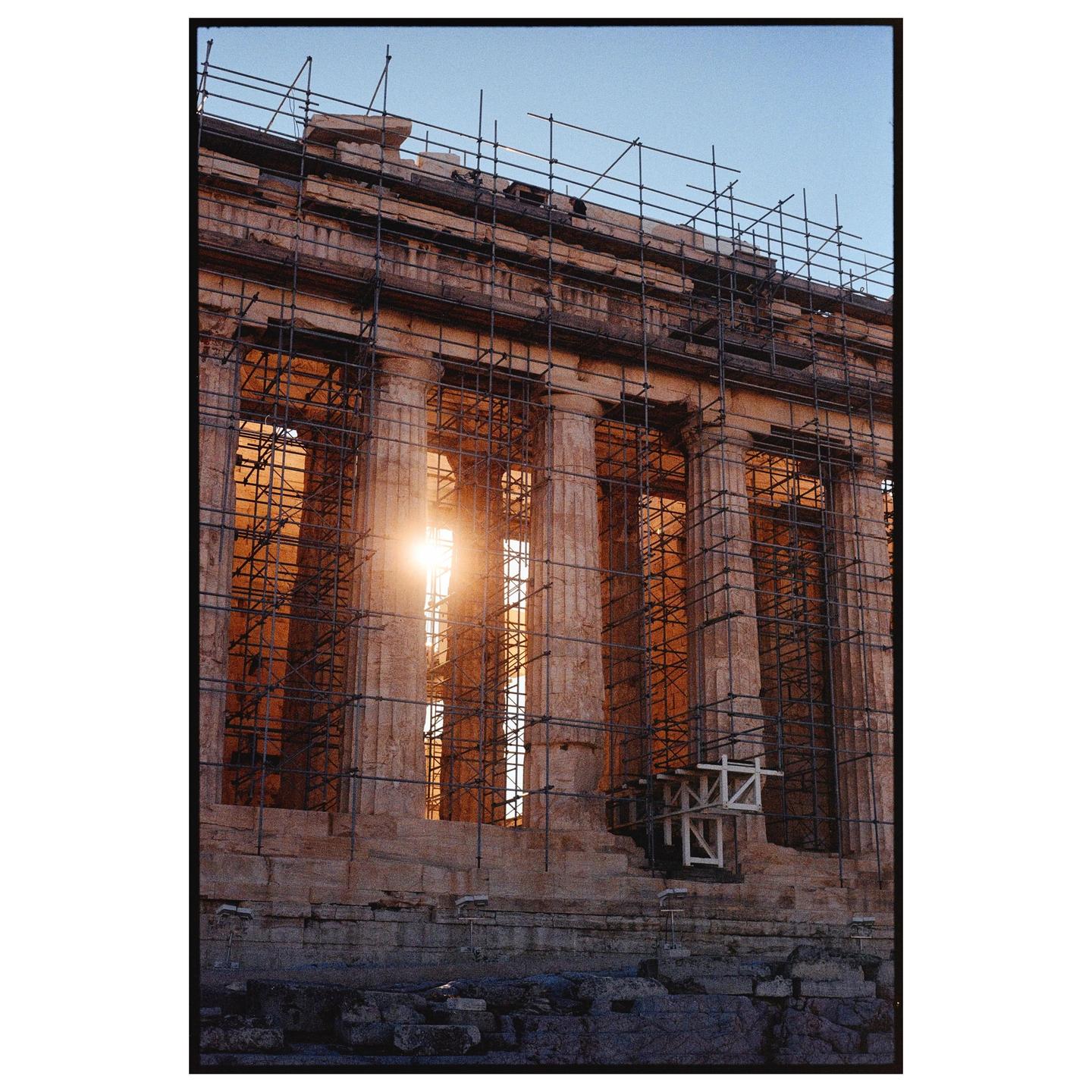 The Parthenon is under construction with scaffolding covering its columns, and the sun shines through an opening.