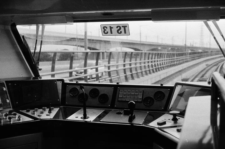 The interior of a train driver's cabin shows the controls and the view through the front window of the tracks ahead.