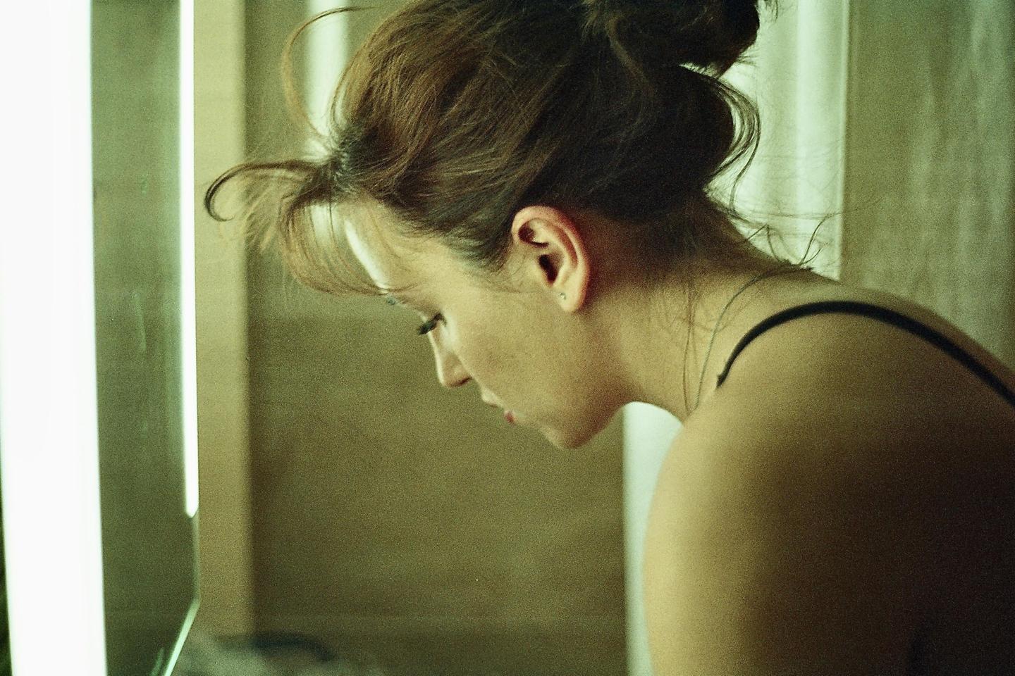 A woman with her hair in a bun looks down, with a bright vertical light source to her left.