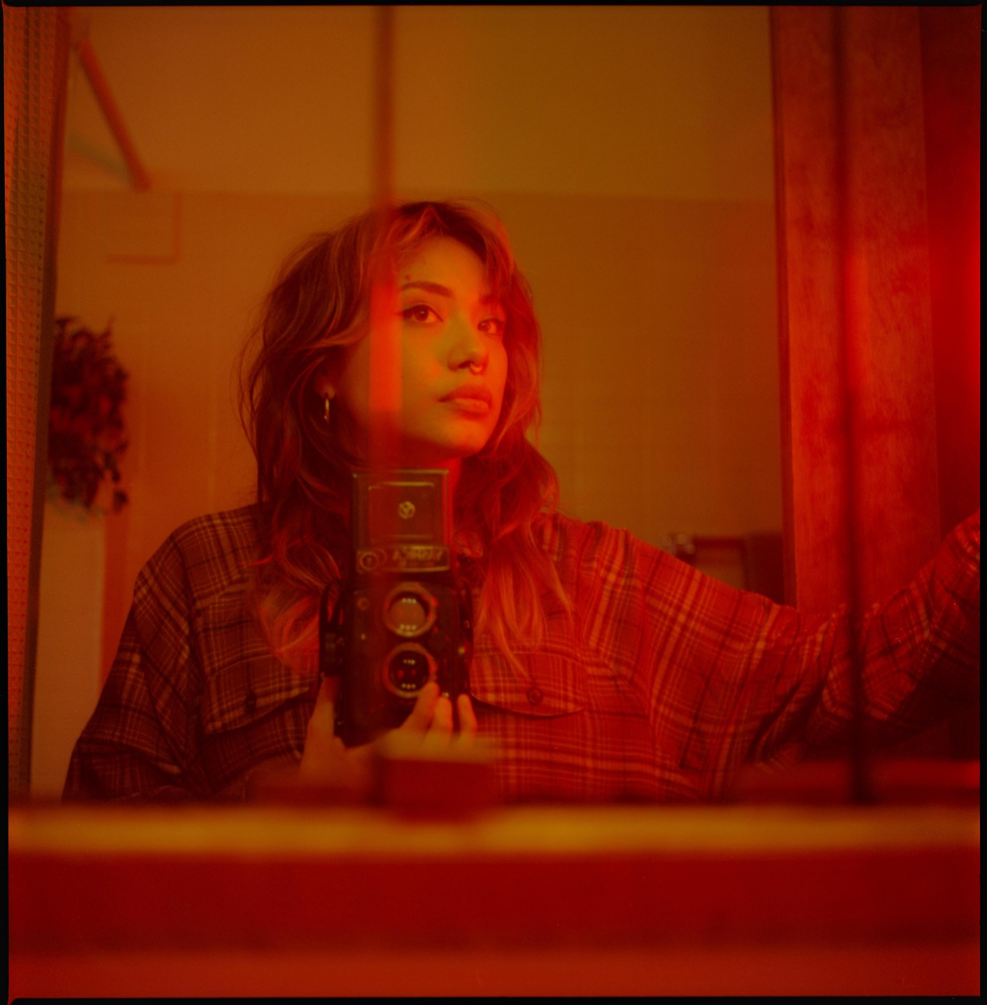 A woman in a plaid shirt takes a self-portrait in a mirror while holding a camera.