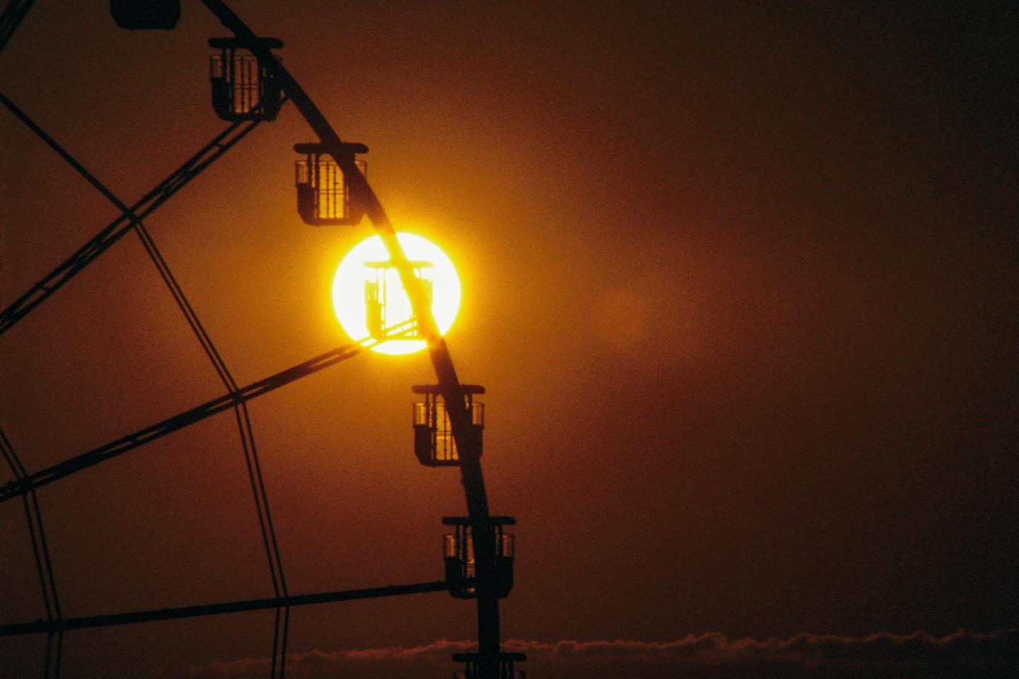The sun is visible behind the silhouette of a ferris wheel.