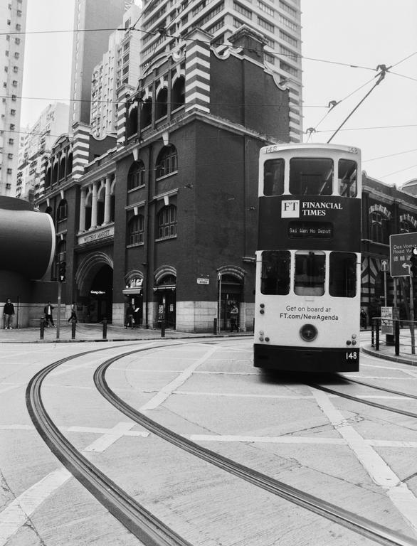 A double-decker tram is turning on a street in front of a large building with arched windows.