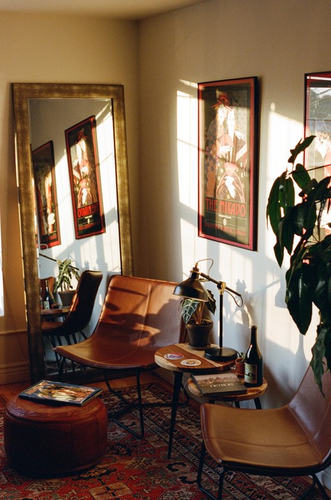 Sunlight streams into a cozy room with leather chairs, a patterned rug, and framed posters.