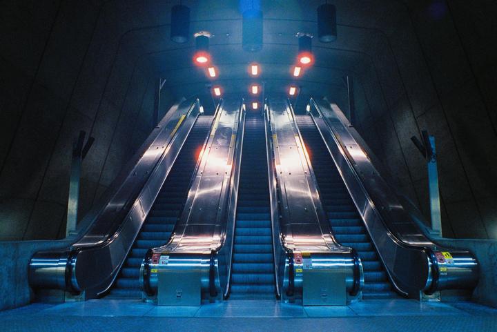 Two escalators ascend into a dark, cavernous space illuminated by red and blue lights.