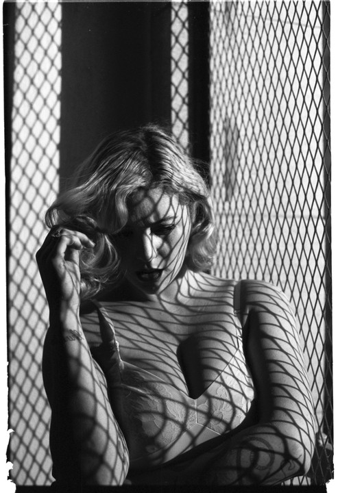 A woman with curly hair and a bra is covered in shadows from a mesh pattern.