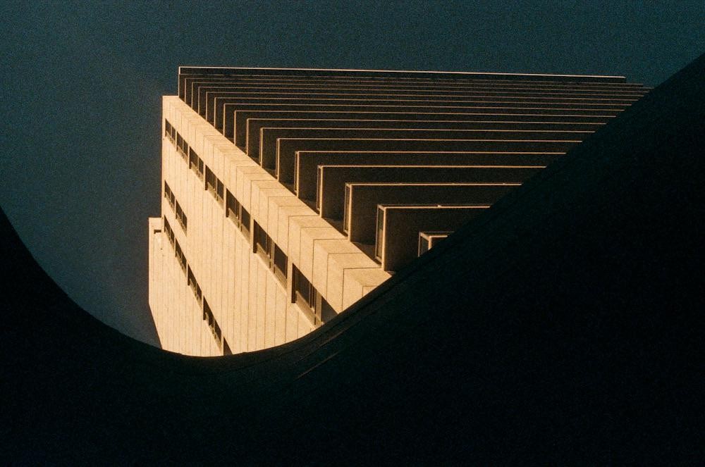 A tall building with many windows is visible from a low angle, with a dark, curved shape in the foreground.