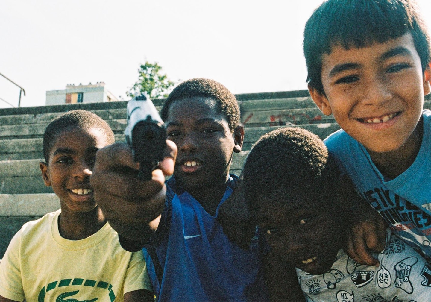 Four boys are posing for a photo on concrete steps, with one boy in the center holding a toy gun towards the viewer.