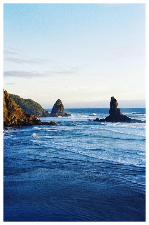 Waves crash against a rocky coastline with two large sea stacks rising from the water.