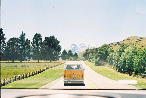 A yellow van drives down a road with mountains in the distance.