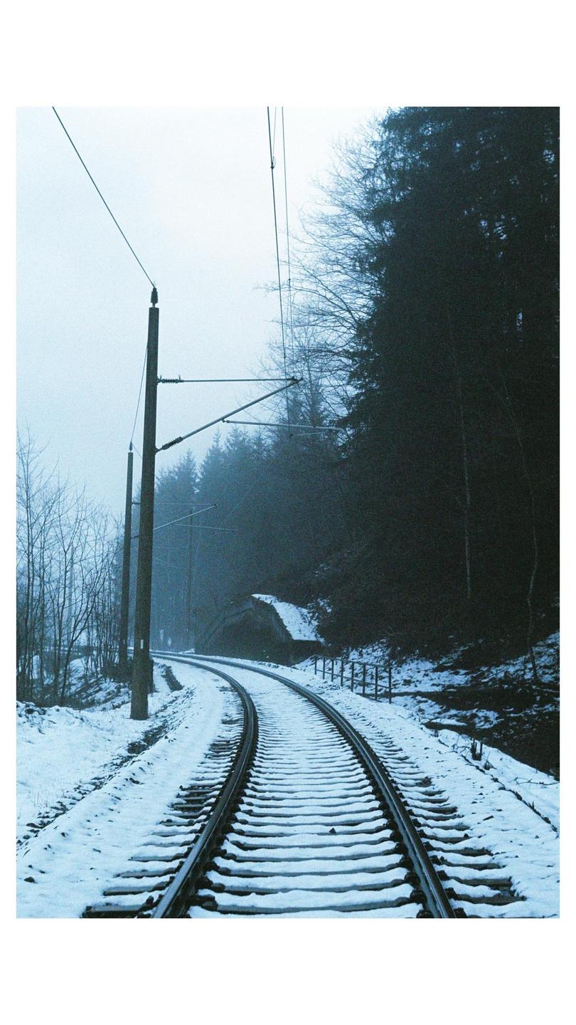 A snow-covered railway track curves through a forest with overhead power lines.