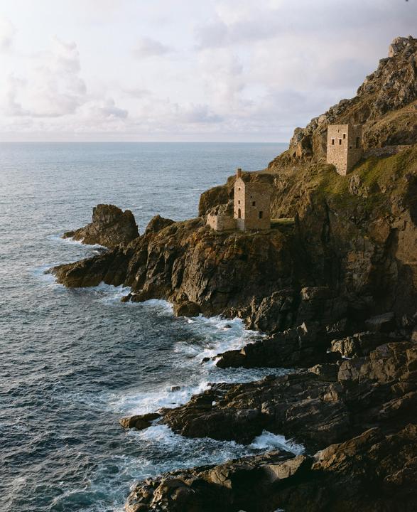 Two stone buildings are perched on a rocky cliff overlooking the ocean.