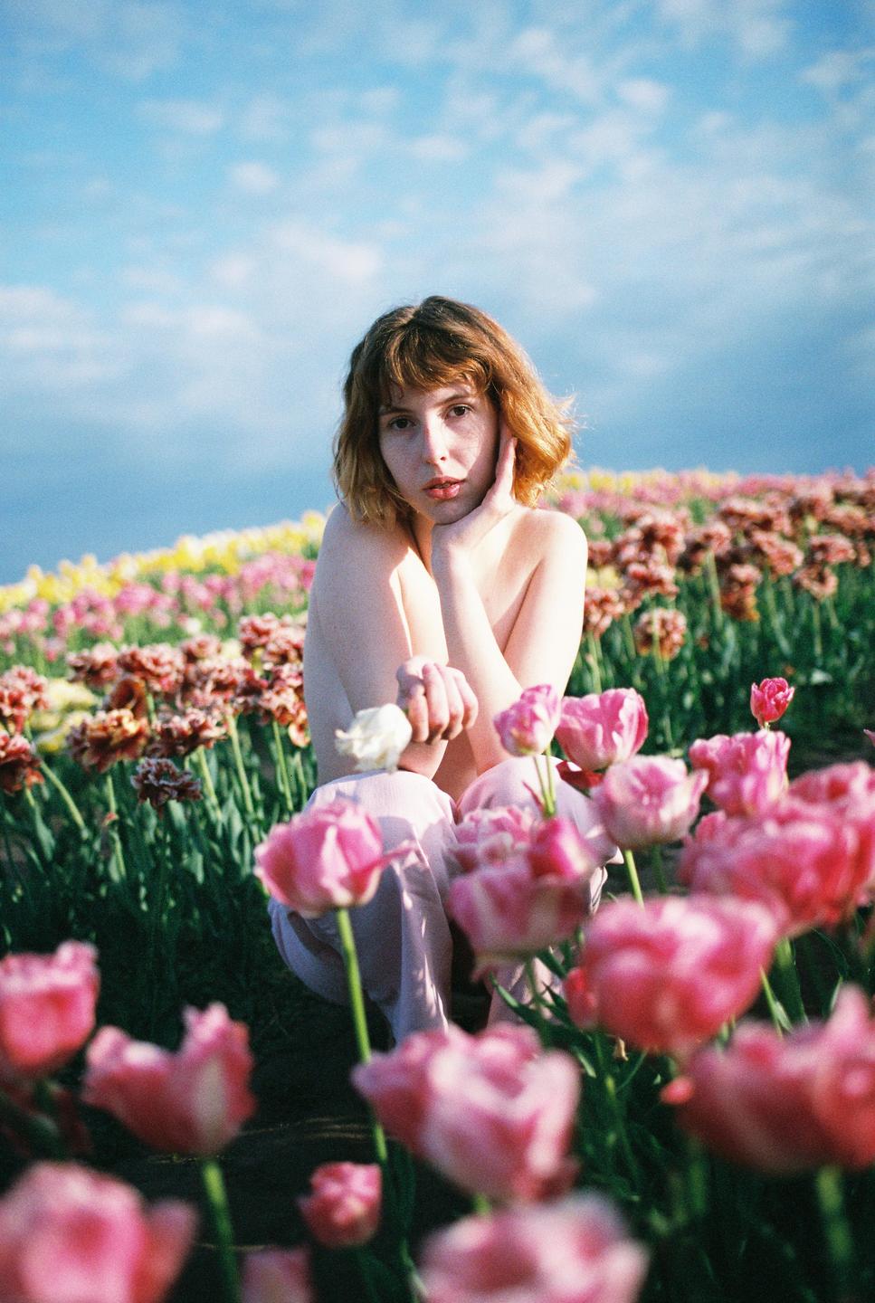A woman kneels in a field of pink and yellow tulips under a blue sky.