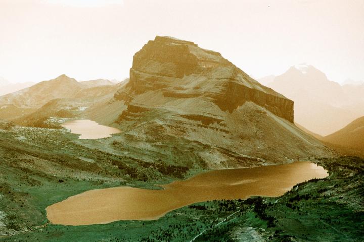 A large mountain overlooks two lakes in a valley with other mountains in the distance.